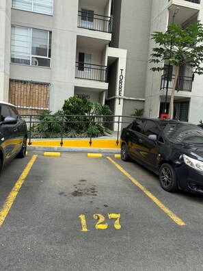 Ein Parkplatz mit zwei Autos, ein Gebäude mit Balkonen und ein Baum.