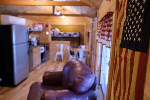 Ein gemütliches Interieur mit Holzboden, einem Essbereich mit Stühlen, einer Küchenzeile mit Kühlschrank und einer amerikanischen Flagge an der Wand.