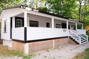 Eine Holzhütte mit überdachter Veranda, einer Treppe und einer Auffahrt mit Kies.