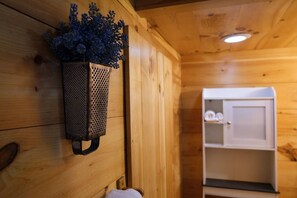 Een houten cabin met een hangende bloempot met blauwe bloemen, een witte kast met handdoeken en een houten bank.