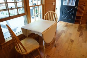 Une pièce avec une table blanche et deux chaises en bois, une fenêtre avec des stores et une porte ornée d’un motif géométrique.