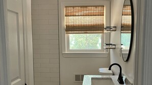 Ein Badezimmer mit Badewanne, Toilette, Waschtisch inklusive Spiegel und einem Fenster mit Jalousien.