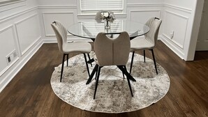 Ein Essbereich mit einem runden Glastisch, vier gepolsterten Stühlen, einem weißen Teppich und weißen Wandverkleidungen.