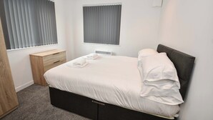 Een slaapkamer met een bed, nachtkastje en een raam met zonwering.