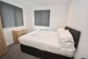 A bedroom with a bed, bedside table, and a window with blinds. - Contemporary 1 Bedroom Apartment in Leeds (Leeds)