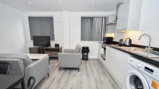 Een moderne keuken met een wasmachine, een eethoek met een tafel en stoelen, een bank en een televisie.