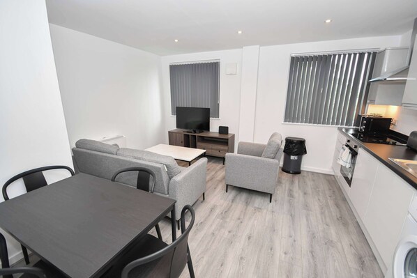 A compact living space with a dining table, sofa, TV, kitchenette, and a washing machine. - Contemporary 1 Bedroom Apartment in Leeds (Leeds)