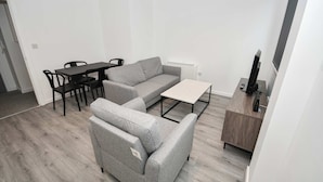 Een moderne woonkamer met een grijze bank, een eettafel met stoelen, een klein wit tafeltje en een houten kast.