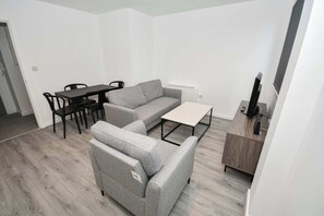 A modern living room with a grey sofa, a dining table with chairs, a small white table, and a wooden cabinet. - Contemporary 1 Bedroom Apartment in Leeds (Leeds)