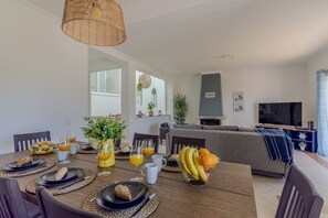 A dining area with a wooden table set for breakfast, a sofa in the background, and a television on the right. - #375 Spacious Townhouse with Pool, BBQ, and Parking (Albufeira)