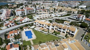 Ett flygbildsbild av ett bostadsområde med vita byggnader, en swimmingpool och en tydlig utsikt över kustlinjen.