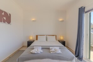A hotel room with a bed, two bedside tables with lamps, a window with curtains, and a towel rack with towels. - #375 Spacious Townhouse with Pool, BBQ, and Parking (Albufeira)