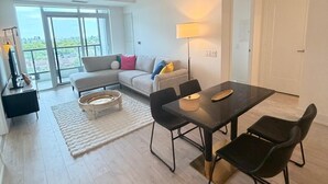 A modern living room with a sofa, dining table, and chairs. There is a large window providing a view of the city. - New Executive Condo Midtown Toronto -  Airport pick up included - Free Parking (Toronto)