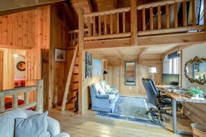 A wooden cabin interior with a loft bedroom, a living area with a sofa and armchair, a desk with a computer, and a dining table. - Lake Muskoka Escape - McVittie Island|Wifi|Firepit (Bracebridge)