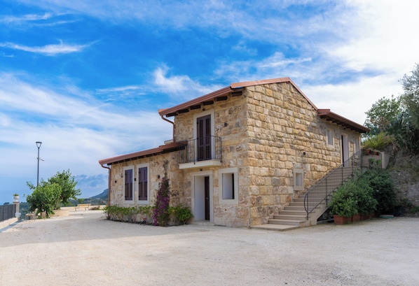 A stone building with a balcony, a staircase, and a gravel driveway.