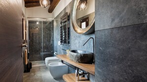 Un baño moderno con cabina de ducha de vidrio, inodoro independiente, tocador de madera con lavamanos de piedra y un espejo grande.