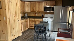 A kitchen with wooden cabinets, a dining table with chairs, a refrigerator, and a stove. - Lake Trout Cottage on the Stunning West Shore of Sebago Lake (Sebago)