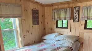 A wooden cabin bedroom with a bed, a window, and a welcome sign. - Lake Trout Cottage on the Stunning West Shore of Sebago Lake (Sebago)