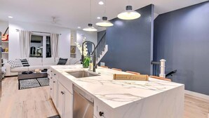 Une cuisine moderne dotée d’un plan de travail en marbre, d’un lave-vaisselle encastré et de luminaires suspendus.