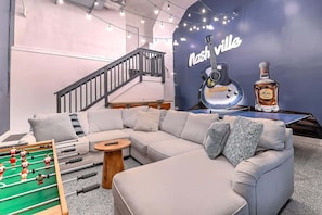 Ein modernes Wohnzimmer mit einer Couch, einem Kicker, einer Treppe und einer Wand mit einer Gitarre und einer Flasche.