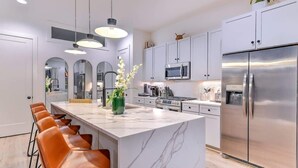 Une cuisine moderne avec des meubles blancs, des appareils en acier inoxydable, un îlot en marbre et des tabourets de bar en cuir.