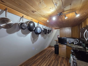 A kitchen with wooden ceiling, hanging pots, a stove, and a trash bin.