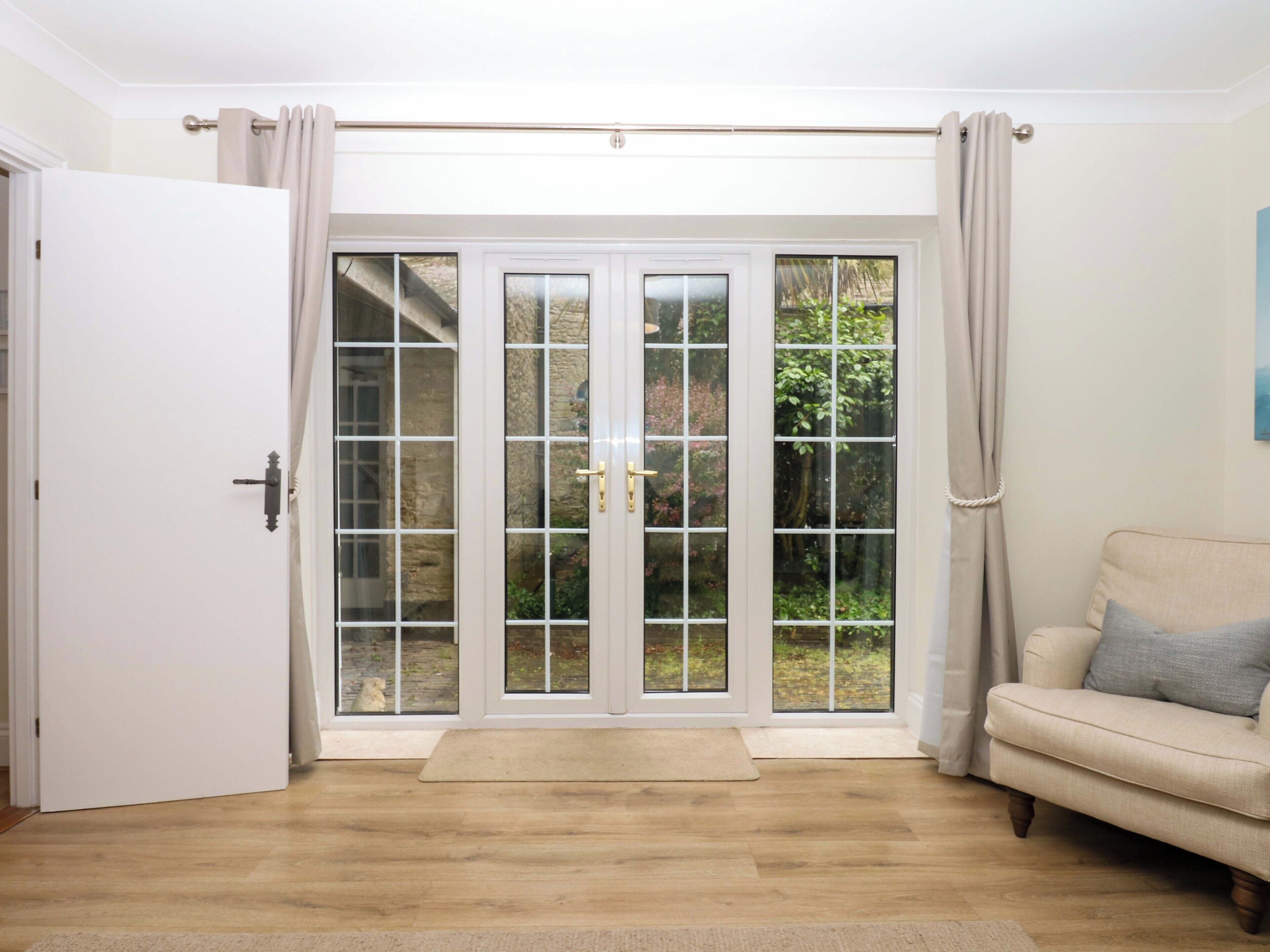 A room with a white door, a beige sofa, a wooden floor, and a view through a glass door.