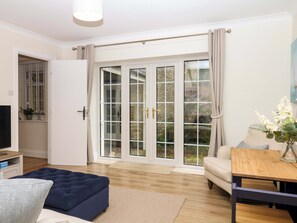 Uma sala de estar com sofá, mesa de centro, TV e porta de vidro deslizante que dá para um jardim.