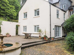 Un bâtiment blanc avec de nombreuses fenêtres, une fontaine en pierre et des plantes en pot.