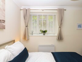 Un dormitorio con cama, ventana con cortinas, radiador y una planta en maceta.