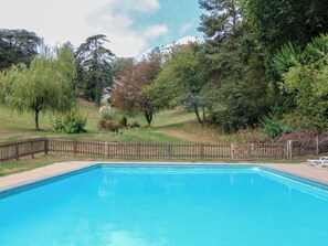 Una piscina rodeada por una valla de madera, con árboles y un césped al fondo.