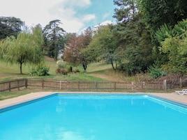 Una piscina rodeada por una valla de madera, con árboles y un césped al fondo.