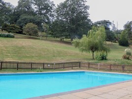Una piscina con cerco de madera, rodeada de césped y árboles.