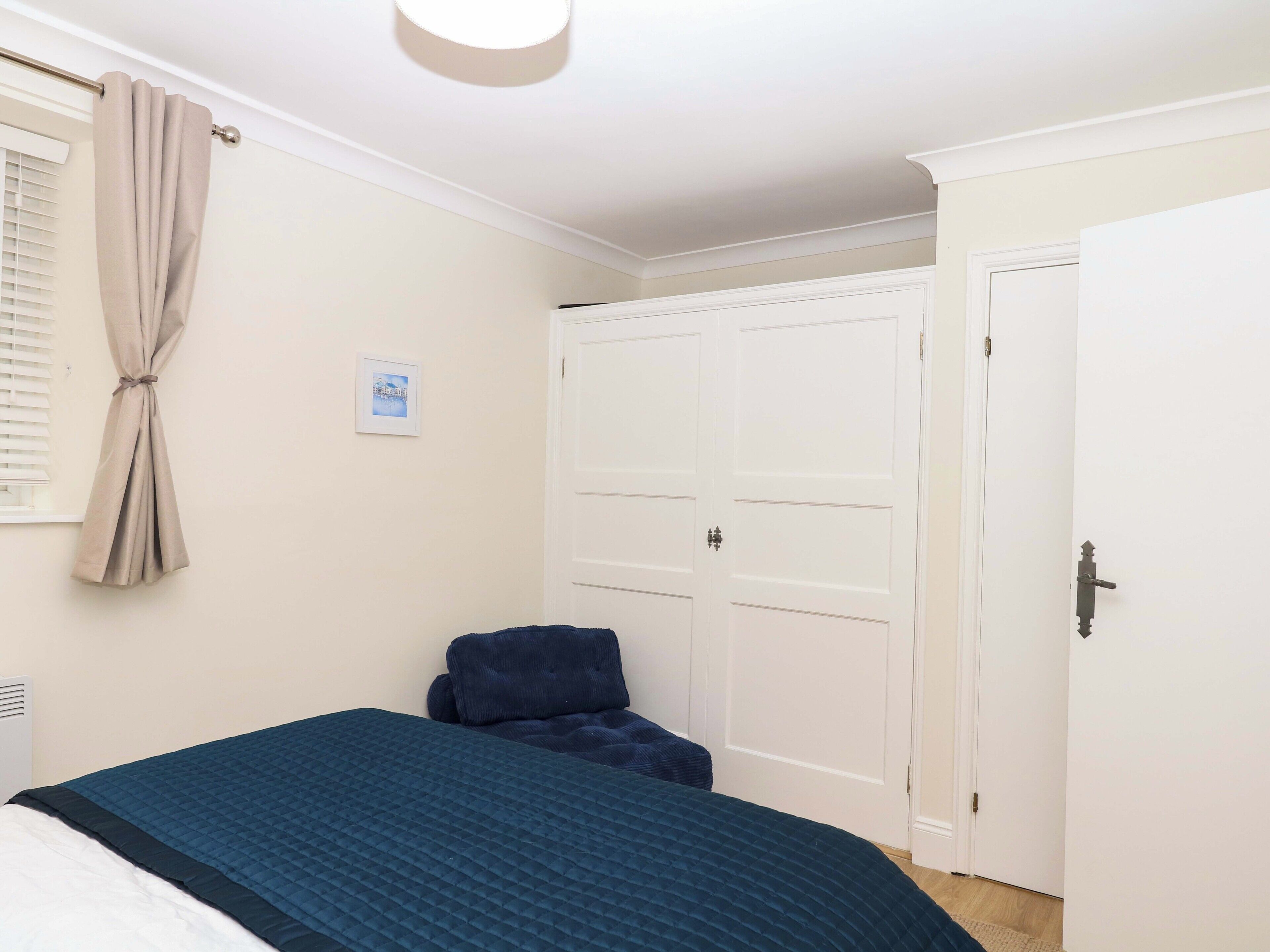 Un dormitorio con cama, ventana con persianas, puerta y radiador fijado a la pared.