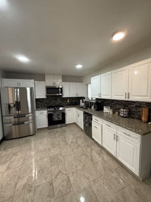 A modern kitchen with white cabinets, stainless steel appliances, and a granite countertop. - Anihouse . (Las Vegas)