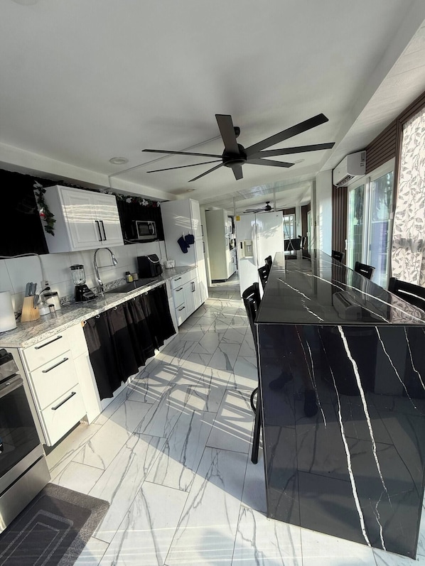 A modern kitchen with a black marble island, white cabinetry, and a ceiling fan. - Anihouse . (Las Vegas)