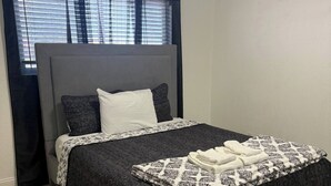 En snyggt bäddad säng med ett mönstrat överkast, en sänggavel och en tavla med en stadsbild ovanför.