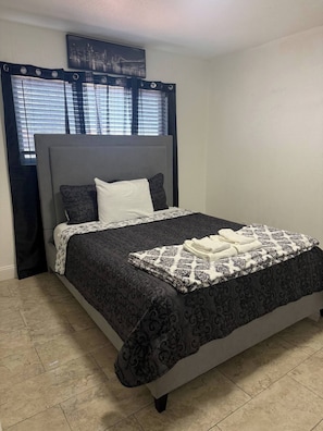 A neatly made bed with a patterned bedspread, a headboard, and a cityscape picture above it. - Anihouse . (Las Vegas)
