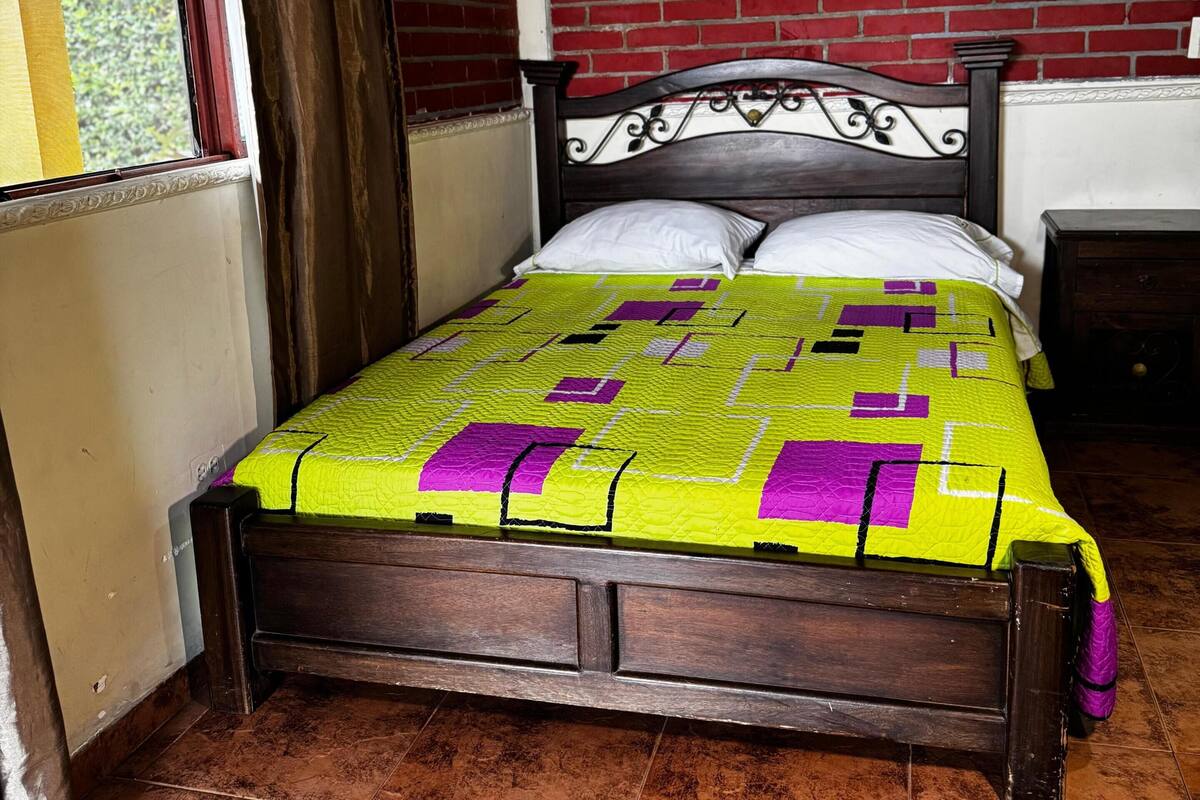 Una habitación con una cama, una ventana con cortinas, una pared de ladrillo y un cuadro.