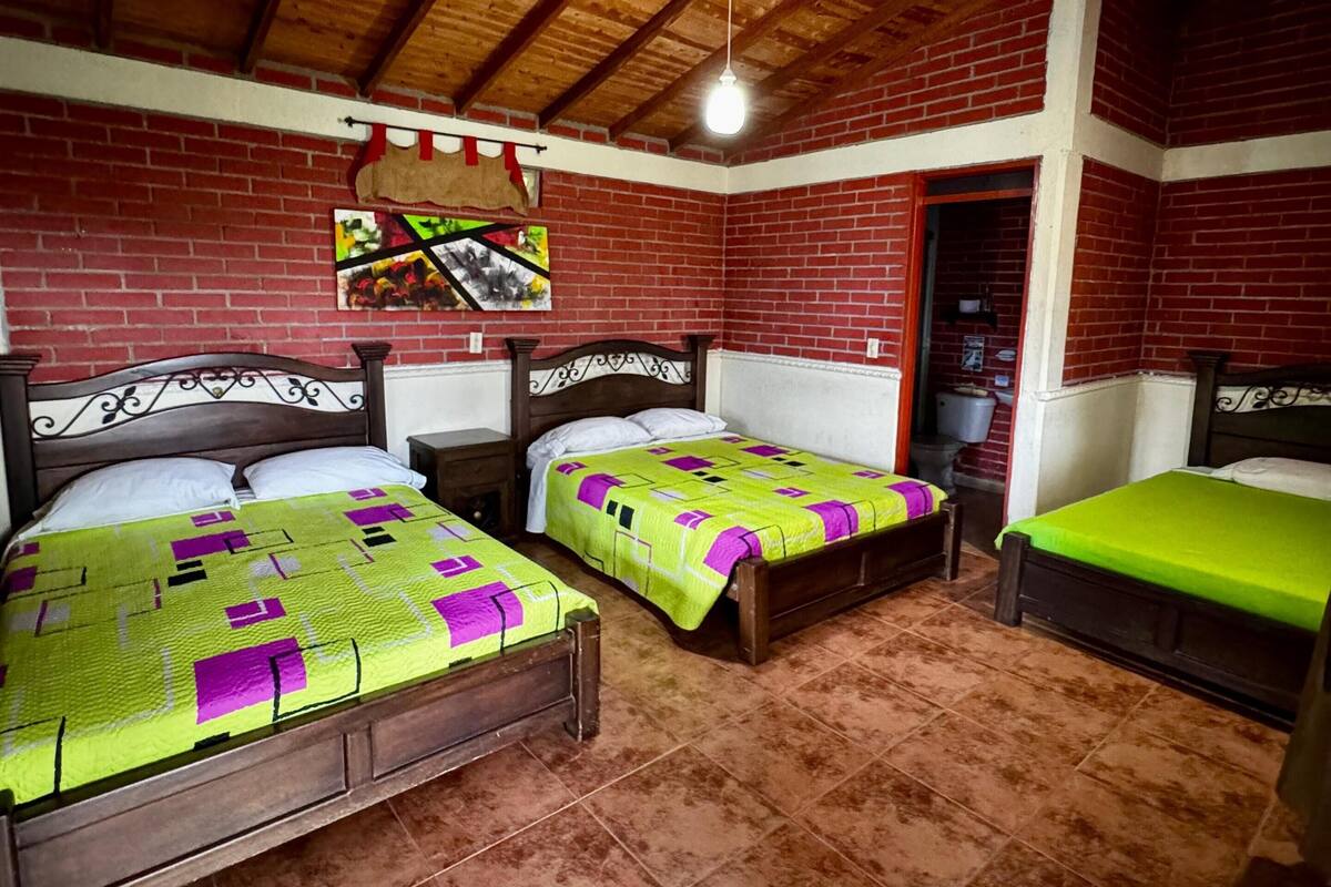 Una habitación con tres camas de madera, una pared de ladrillo, una lámpara colgante y un cuadro.