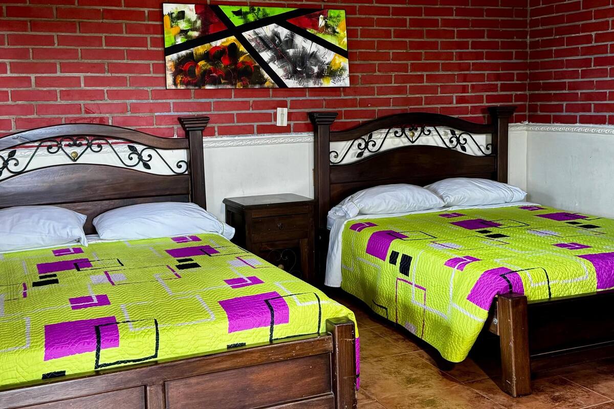 Una habitación con dos camas de madera, una pared de ladrillo, una lámpara colgante y un cuadro.