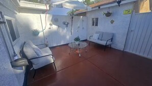 A covered patio with a white wall, a glass table, two white chairs, and a hanging plant. - Ani place  . (Las Vegas)