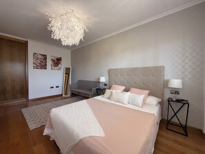 A bedroom with a large bed, a hanging light fixture, a sofa, and a mirror.