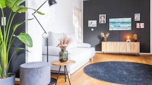 En moderne stue med en grå sofa, et rundt gulvtæppe, et sofabord med en vase, en gulvlampe og et træskab med kunstværker.