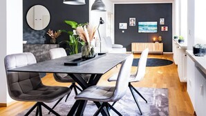 Et moderne spiseområde med et bord i mørkt træ, grå polstrede stole og en grå måtte.