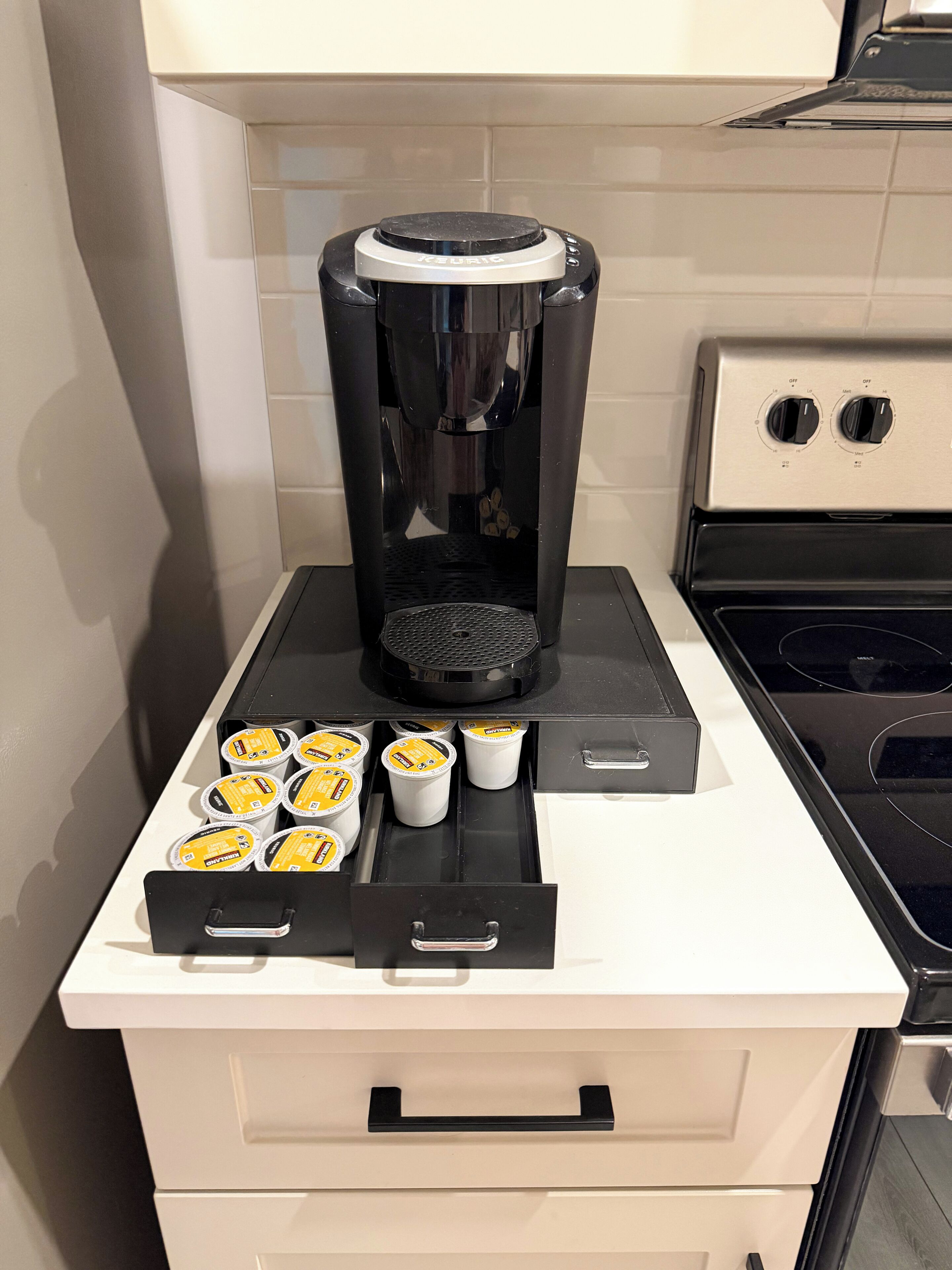 Una cocina con cafetera Keurig, estufa y un cajón con cápsulas de café.