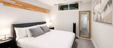 A modern bedroom with a bed, bedside tables, a mirror, and a ceiling light.