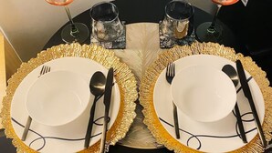 Una mesa de comedor con dos juegos de platos, cubiertos y vasos, cada juego con una copa de vino.