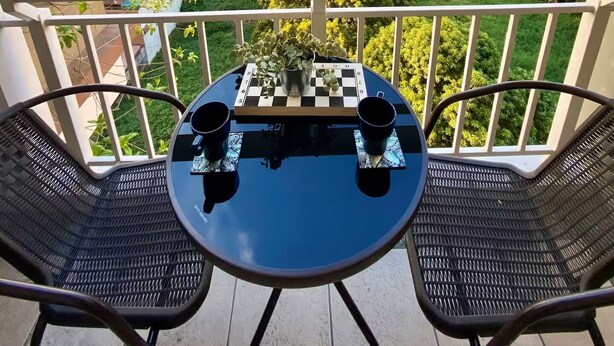 Un balcón con mesa y sillas, un tablero de ajedrez y vistas a la ciudad.