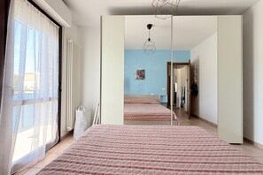 Una habitación con una cama grande, una ventana con cortinas traslúcidas, un radiador y una lámpara colgante.